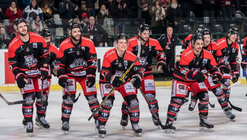 Équipe de hockey des Boxers de Bordeaux, souriante et fière sur la glace. Maillots rouges et noirs avec sponsors Voltéa, Bauer, Carrefour.
